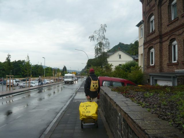 Mit Langstock und Gepäcktrolli auf dem Gehweg in Braubach am Rhein bei Regen