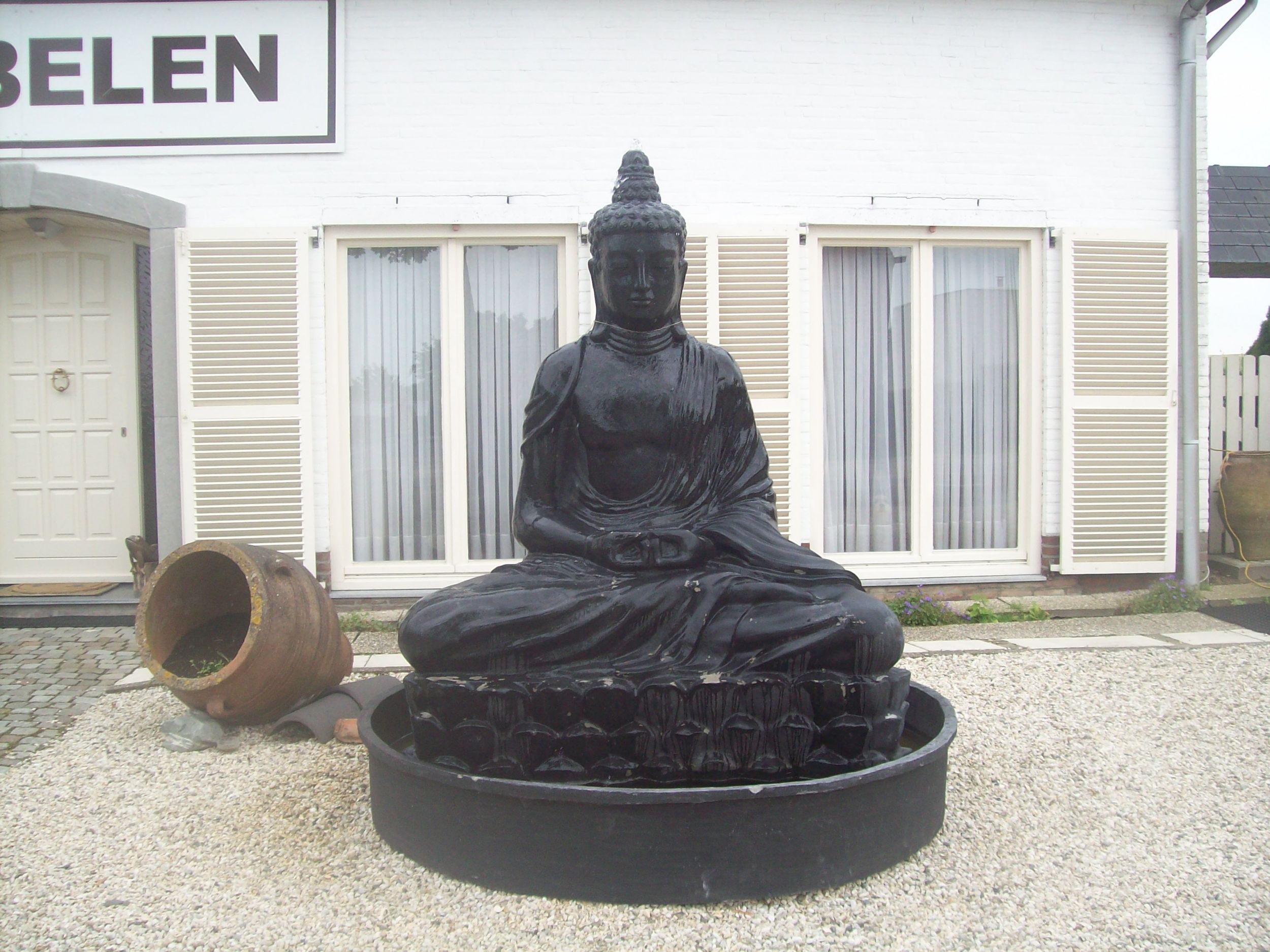 Lebensgroße Buddha-Figur in einem Vorgarten in ländlicher Umgebung